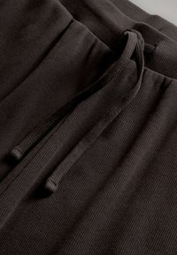 Mustade soonikuga riidest dressipükste vöökohal lähedalt vaadatuna, millel on seotud nöör.