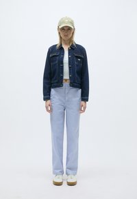 Tamna plava traper jakna, bijeli kratki top, svijetloplave široke hlače, zeleni šešir, bijele tenisice s smešnim đonom, minimalistički dizajn.