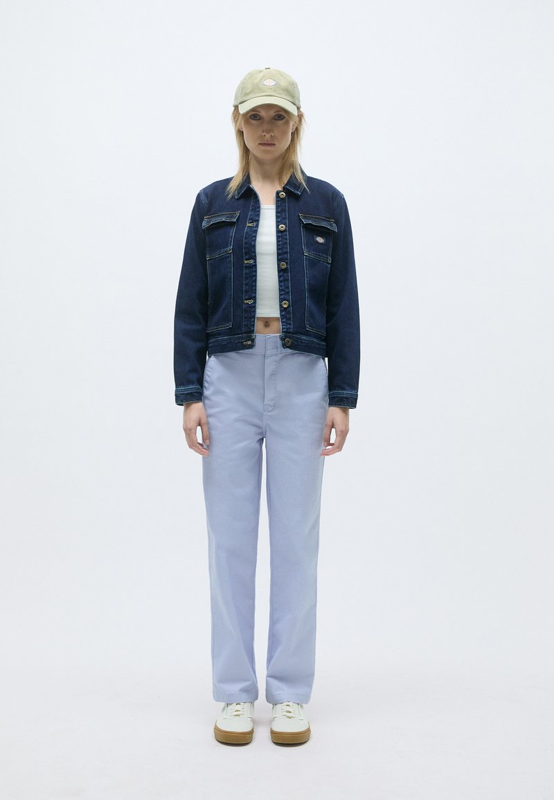 Donkerblauwe denimjack, witte crop top, lichtblauwe wijde broek, groene pet, witte sneakers met gomrubberen zool, minimalistisch ontwerp.