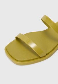 Grønne sandaler med to glansfulde, flade stropper, en firkantet tådesign og en tekstureret sål. Lavet af et glat, syntetisk materiale.
