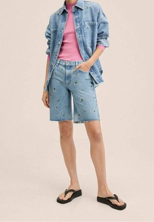 Blaue Jeansjacke und Shorts, beide mit floralem Stickdesign. Darunter ein hellrosa geripptes Top. Schwarze Flip-Flops, lässige Passform, ausgefranster Saum bei den Shorts.