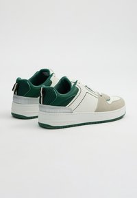 Zapatillas con una parte superior blanca y verde que presenta detalles de malla, acentos de ante, una suela texturizada y un cuello acolchado distintivo.
