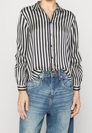 Person wearing a black and white vertically striped button-up shirt tucked into high-waisted blue jeans with a leather belt.