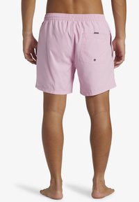 Bañador corto rosa con cintura elástica, bolsillos laterales y traseros, y una textura ligera y suave.