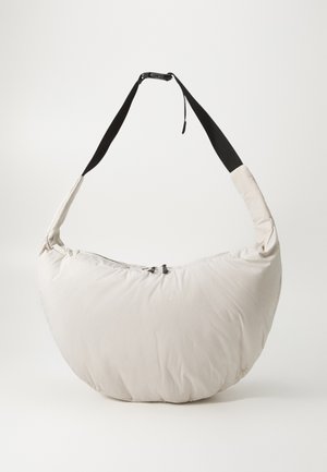 Light beige padded shoulder bag with a curved, half-moon shape. Black strap, zipper closure, and subtle logo on the front. Soft texture.