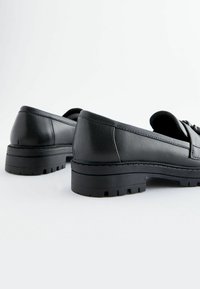 Mocassins noirs en cuir texturé avec une semelle épaisse et crantée. Présente des bords lisses et un minimum de coutures. Design classique avec des accents subtils.