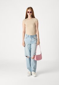 Top beige à rayures à manches courtes, jeans baggy déchirés bleu clair, baskets blanches, sac à main rose et lunettes de soleil cat-eye roses.