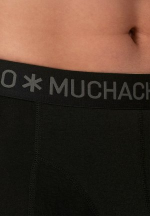 Crni pamučni bokserice s širokim crnim pojasom na kojem je sivo slovo "MUCHACHO". Tkanina izgleda glatko s ravnim šavovima.