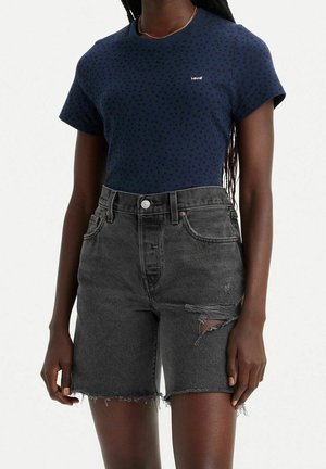 Osoba nosząca granatowy t-shirt Levi’s z subtelnym nadrukiem i czarne, zniszczone szorty jeansowe z wysokim stanem i postrzępionymi brzegami.