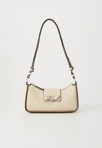 Beige læderhåndtaske med et buet design, sorte accenter og en metal "Karl"-logo foran. Har en justerbar skulderrem.