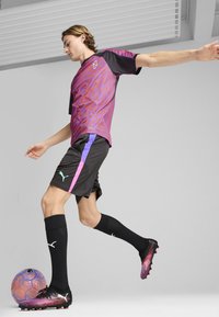 Conjunto de ropa deportiva Puma que incluye una camiseta de patrón púrpura y negro, pantalones cortos negros con acentos en rosa y púrpura, y calcetines negros con logo.