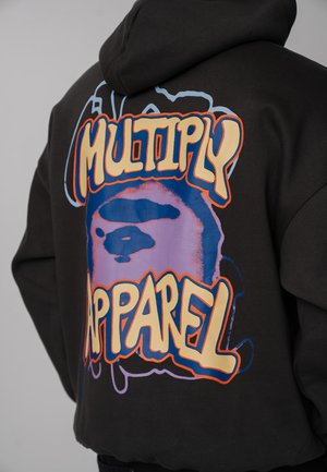 Felpa nera con cappuccio, con grafica colorata e testo audace "Multiply Apparel" sulla schiena, indossata da una persona vista di spalle.