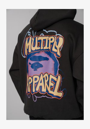 Black hoodie with colorful graphic art and bold text reading "Multiply Apparel" on the back, worn by a person facing away.
