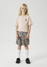 Svetlo roza majica s srcem v črno-belem zebra vzorcu in črno zebra vzorčasto krilo. Črne čevlje in bele nogavice do kolen dopolnjujejo obleko.