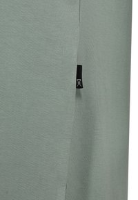 Nærbillede af salviegrønt stof med et sort mærke med en hvid geometrisk logo syet ind i en søm.