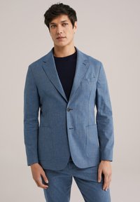 Heledsinine meesteri blazer tekstureeritud kangast, ühe nupuga kinnitamine, klapid, kaks eesmist taskut, kantud tumesinise särgi peal.