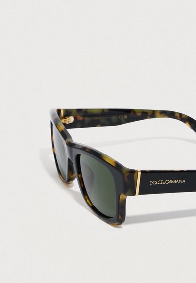 Sončna očala z vzorcem želvje lupine, z debelim plastičnim okvirjem v temno rjavih in zelenih odtenkih. Imajo temna stekla in zlato barvan logotip kot poudarek.