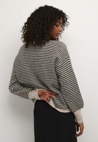 Pull en tricot gris et beige, avec un motif à pois, des épaules tombantes et des poignets côtelés. Texture douce et design décontracté.