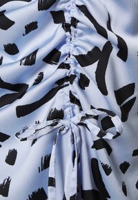 Ljusblått tyg med svarta abstrakta mönster, som har en rynkad textur och band. Materialet verkar mjukt och något texturerat.