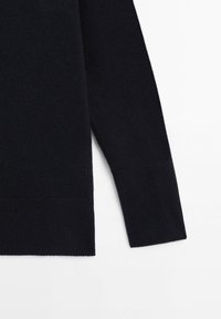 Manche et partie inférieure d'un pull noir en maille à manches longues avec poignets et ourlet côtelés sur fond blanc.