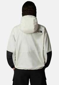 Biała, lekka kurtka z kapturem, czarne akcenty na rękawach oraz logo The North Face na górnej części pleców. Gładka tekstura, casualowy krój.