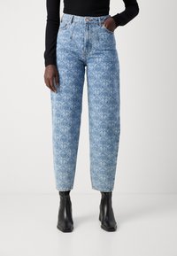 Light blue high-waisted jeans with a geometric pattern, tapered leg, and dark stitching. Worn with black heeled ankle boots.
