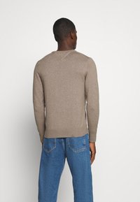 Brauner Strickpullover mit Rundhalsausschnitt und gerippten Bündchen, kombiniert mit blauen Denim-Jeans. Der Stoff wirkt weich mit einer dezenten Textur.