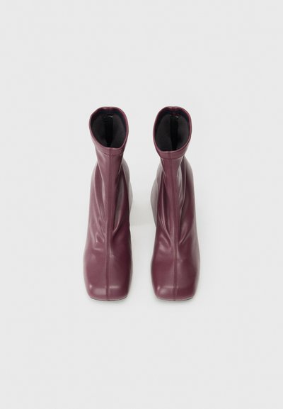 Bottes chevilles bordeaux en cuir lisse au design effilé, dotées d'ouvertures élastiques et de détails de plis subtils.