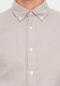 Sivá košeľa na gombíky vyrobená z mäkkej látky, s rozšíreným golierom, šiestimi gombíkmi na prednej strane a textúrovaným povrchom.