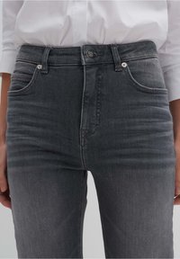 Jeans de mezclilla gris con cintura de altura media, bolsillos frontales y cierre de botón. La tela tiene un acabado ligeramente texturizado.