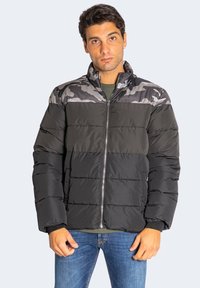 Schwarze Puffjacke mit grauen Camouflage-Akzenten, ausgestattet mit einem Stehkragen, einem Reißverschluss und einem gesteppte Design zur Isolierung.