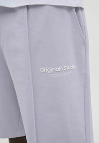 Lila bomullsshorts med sidofickor, med texturerat tyg och tryckt logotyp "Originals Studio" i vitt på vänster ben.