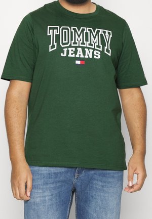 T-shirt verde in cotone con la scritta "TOMMY JEANS" in bianco, accompagnata da un piccolo logo rettangolare rosso, bianco e blu. Maniche corte e colletto rotondo.