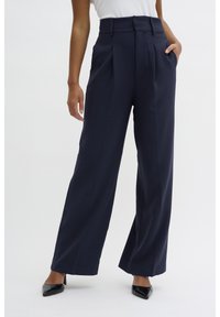 Navy wide-leg trousers featuring a high waist, pleats, and a smooth texture, paired with black pointed toe heels.