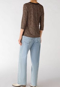 Haut à imprimé léopard marron avec manches trois-quarts, associé à un jean large bleu clair. Le haut présente un col arrondi et des fentes latérales.