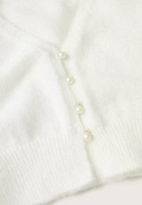 Měkká bílá pletenina s perlami podobnými knoflíkovými ozdobami uspořádanými do svislé linie.