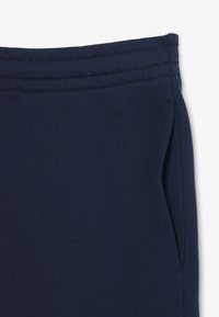 Pantaloni della tuta blu navy in morbido misto cotone, con vita elasticizzata e tre cuciture orizzontali, e tasche laterali. Texture liscia.