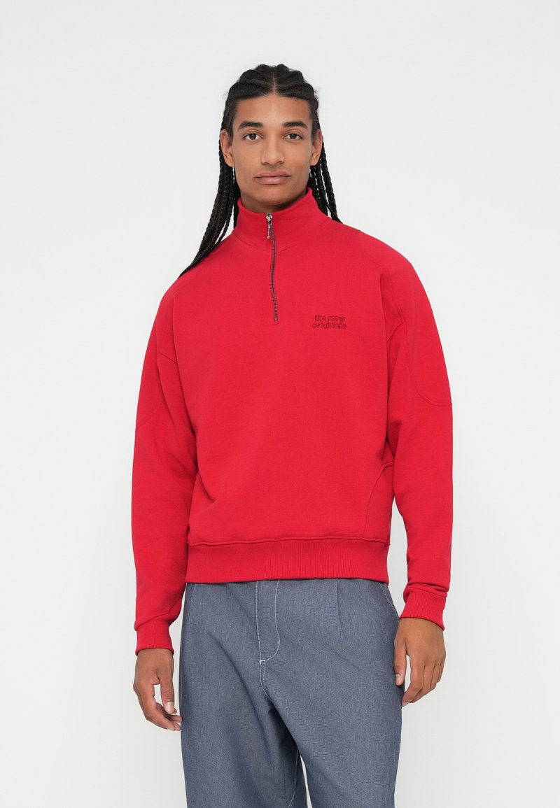 Sudadera roja con cremallera y cuello alto, puños y bajo acanalados, con un pequeño logo negro en el pecho y textura suave.