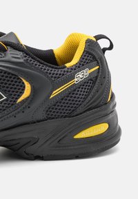 Černá a žlutá atletická bota s prodyšným svrškem, polstrovaným límcem a logem "ABZORB" na patě. Jemné designové detaily a texturovaná podešev.