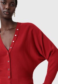 Cardigan rosso lavorato a maglia con scollo a V profondo e dettagli in bottone argentato. Presenta maniche oversized e orlo a costine per una vestibilità rilassata.