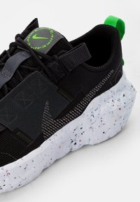 Black and grey Nike sneaker with green accents, textured upper, speckled white sole, and pull tab on heel.