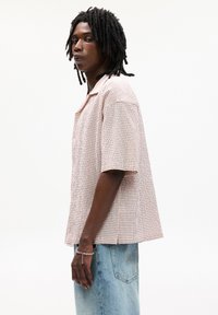 Kortærmet skjorte i et lyserødt og hvidt ternet mønster, med en klapkrave og løs pasform. Båret med lyseblå denim.