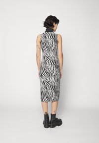 Abito a stampa zebra in bianco e nero con colletto alto, silhouette aderente e lunghezza midi, abbinato a stivali neri chunky.