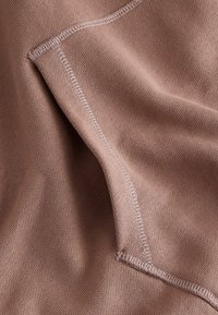 Soft, light brown fabric with a smooth texture and visible stitching detail. Features a folded edge and subtle stretch.