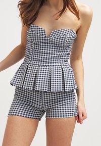 Top senza maniche in gingham blu e bianco con un busto aderente e un peplum svasato, abbinato a pantaloni corti coordinati con una vestibilità sartoriale.