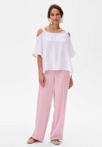 Biała bluzka bez ramiączek z koronkowymi paskami, zestawiona z jasnoróżowymi spodniami w szerokie nogawki i miękkimi różowymi butami, wykonana z gładkiego, lekkiego materiału.