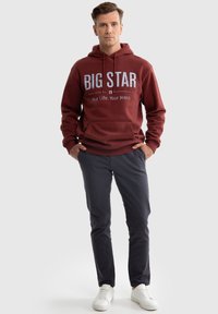 Weinrote Kapuzenjacke mit großen "BIG STAR"-Buchstaben, Fronttasche, kombiniert mit dunkel gemusterten Hosen und weißen Sneakers. Einfaches, lässiges Design.