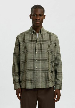 Zaļš taisnā līnija pogājams krekls, izgatavots no teksturēta auduma; tam ir pogājama apkakle un garas piedurknes, ar brīvu piegriezumu un slēptām pogām.