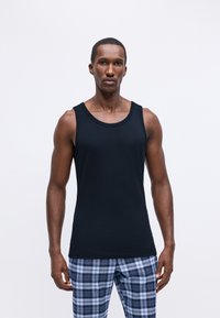 Μαύρο αμάνικο μπλουζάκι με στρογγυλή λαιμόκοψη, φτιαγμένο από λεία ύφανση; το μοντέλο έχει συνδυάσει με γαλάζιο και λευκό καρό πυτζάμα παντελόνι. Απλός σχεδιασμός, χωρίς σχέδια.