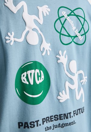 Dve biele abstraktné postavy a zelený kruh s nápisom "RVCA" na modrej látke, zelený atómový symbol s nápisom "dancing heal" a text "MINULOSŤ. PRÍTOMNOSŤ. BUDÚCNOSŤ."